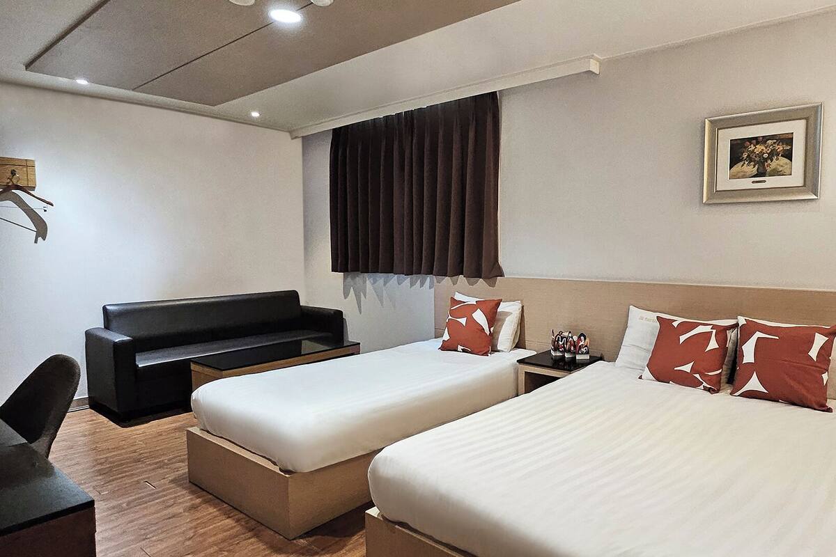 A hotel room with two beds, a sofa, a desk, and a painting on the wall.