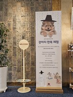 Un área de recepción con pared de ladrillo, un letrero de bienvenida, una planta en maceta y un tablón vertical con ilustraciones y texto.