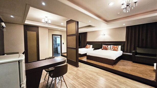 Une chambre d’hôtel avec un bureau, deux lits, un miroir et un lustre.