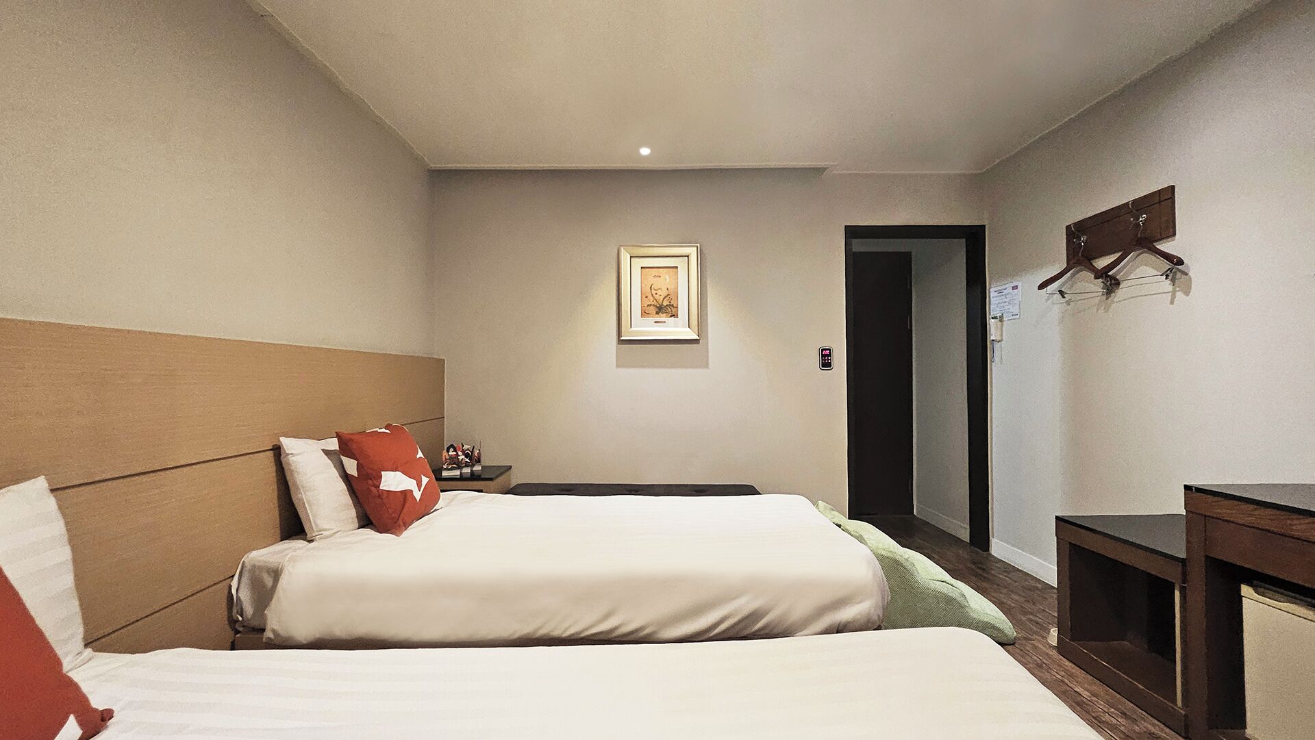 Habitación de hotel con dos camas, una mesita de noche, un cuadro enmarcado en la pared y una puerta que da a otra habitación.