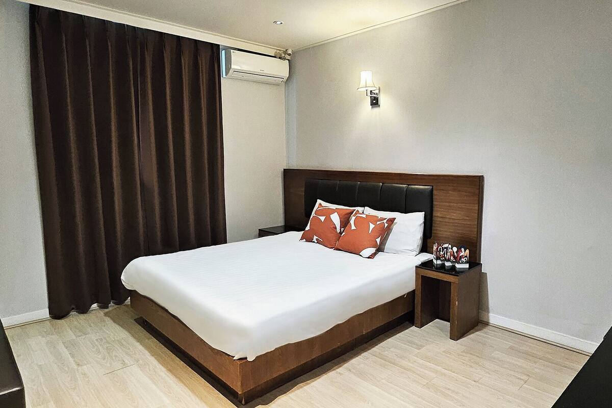 A hotel room with a large bed, a nightstand, a lamp, and a window with curtains.
