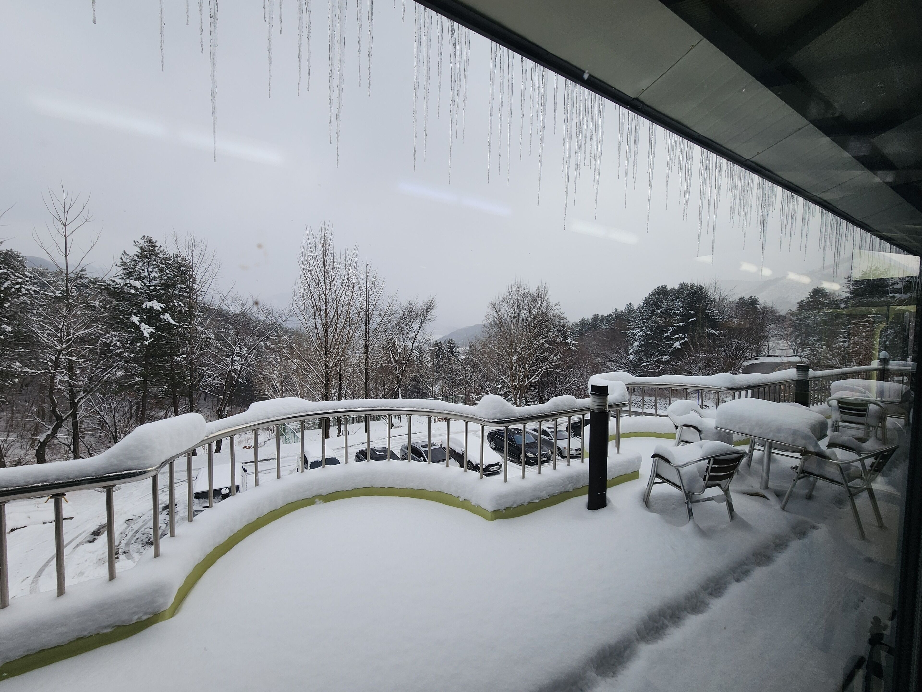 Een besneeuwde buitenruimte met een metalen hekwerk en besneeuwde stoelen.