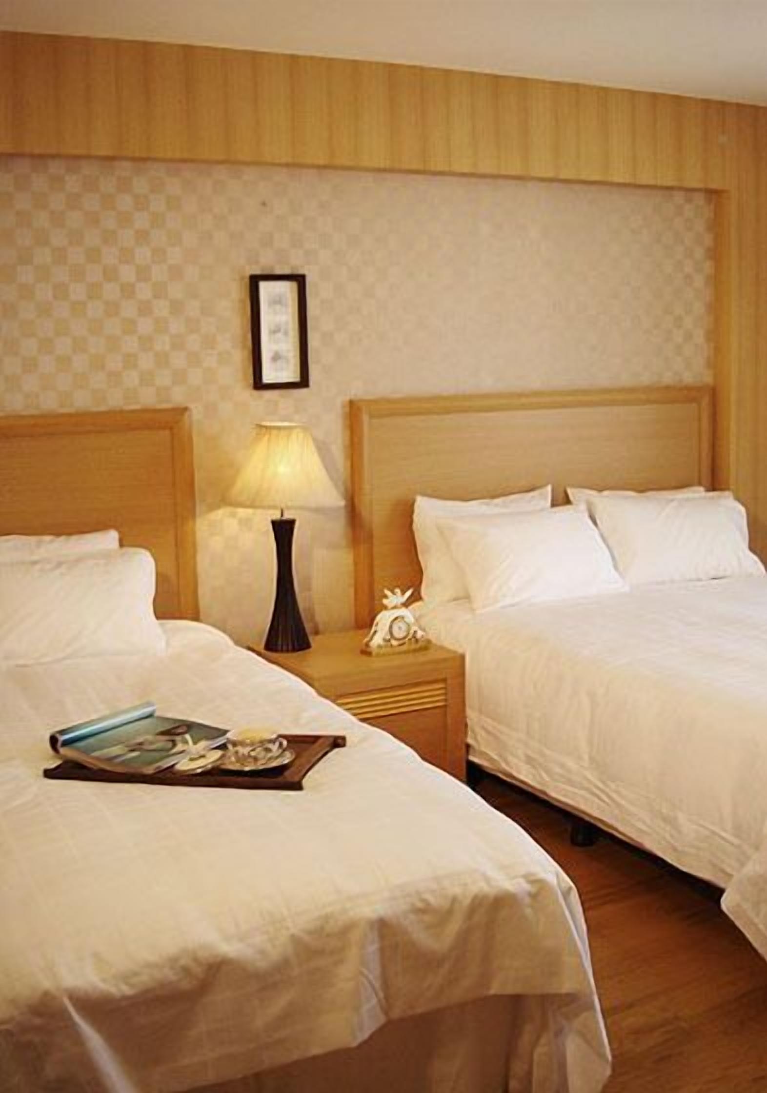 A hotel room with two beds, wooden headboards, a nightstand with a lamp, and a framed picture on the wall.
