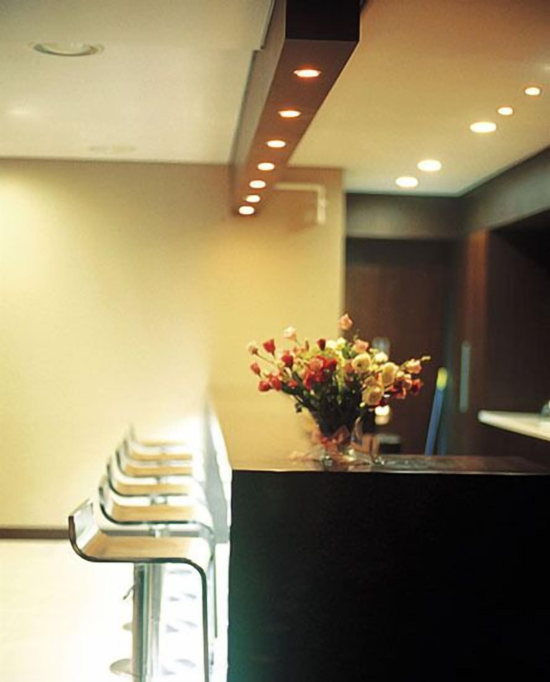 A reception area with a counter, a vase of flowers, and a row of bar stools.