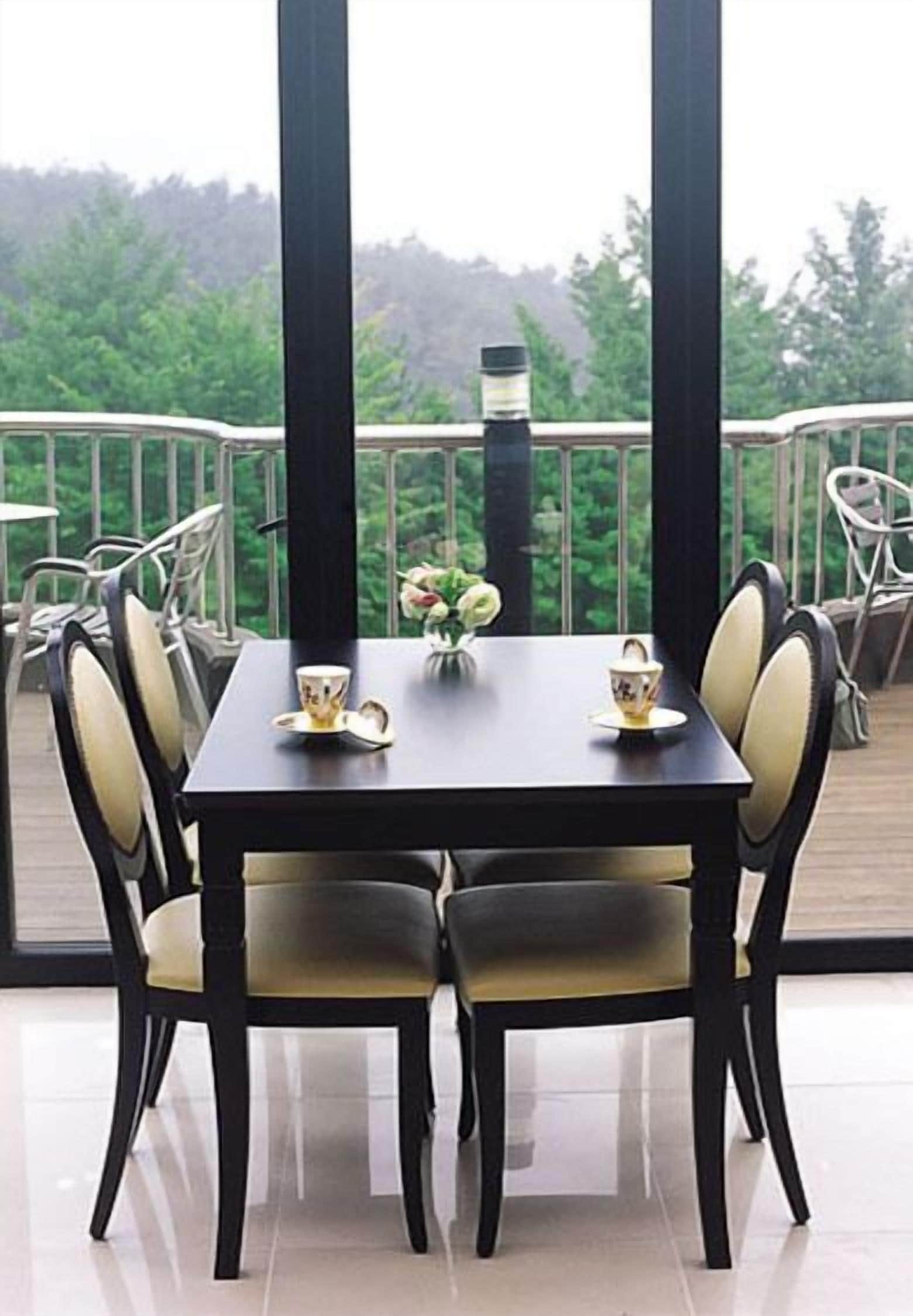 A dining table with four chairs, a vase with flowers, and a bottle on the table.