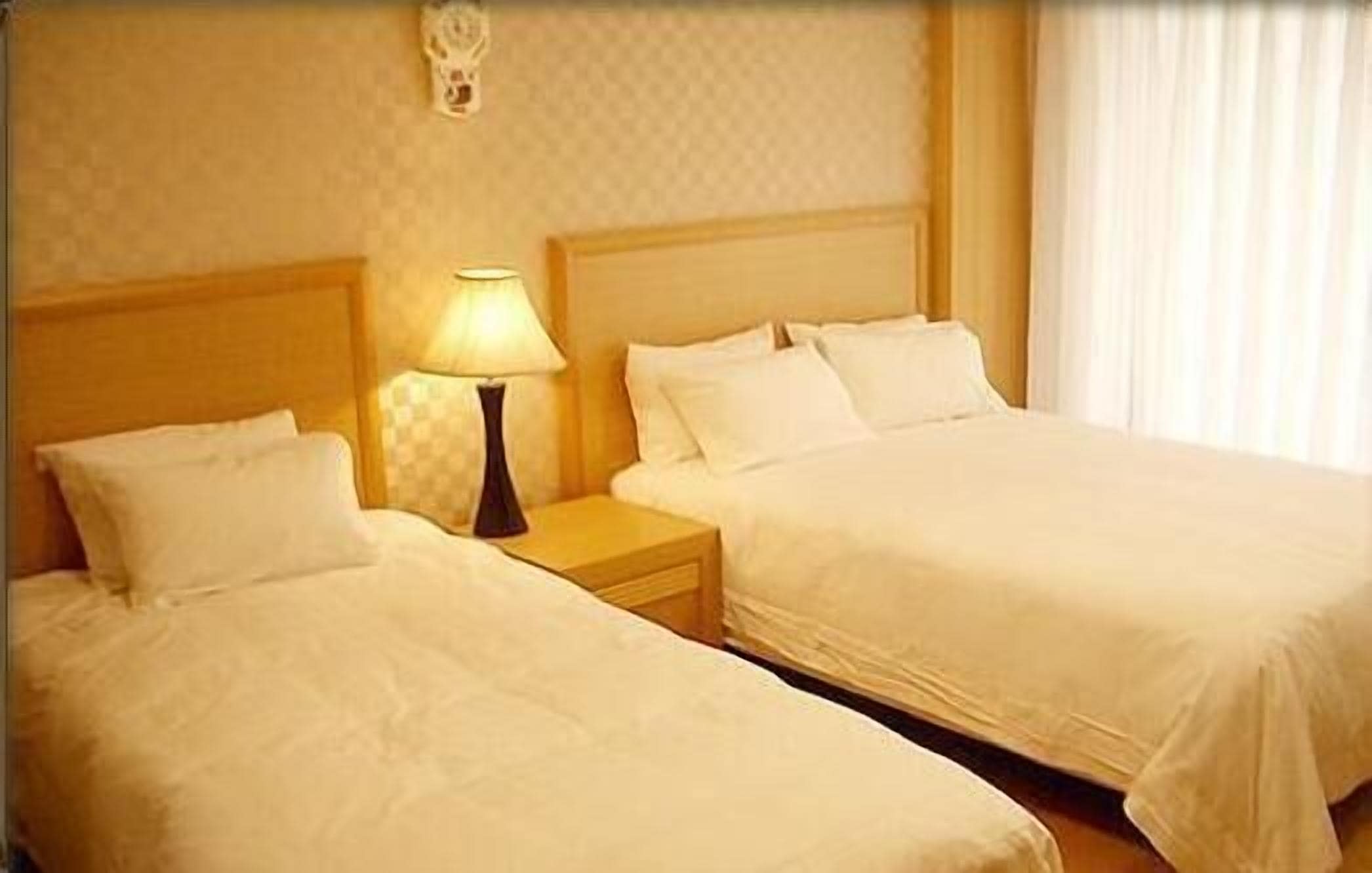 A hotel room with two single beds, a nightstand with a lamp, and a decorative wall piece.