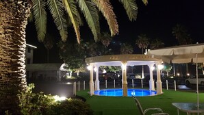 Una pérgola con piscina, rodeada de follaje y palmeras.