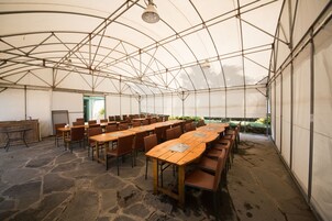 Una gran carpa con suelo de piedra, varias mesas y sillas, y una puerta que da al exterior.