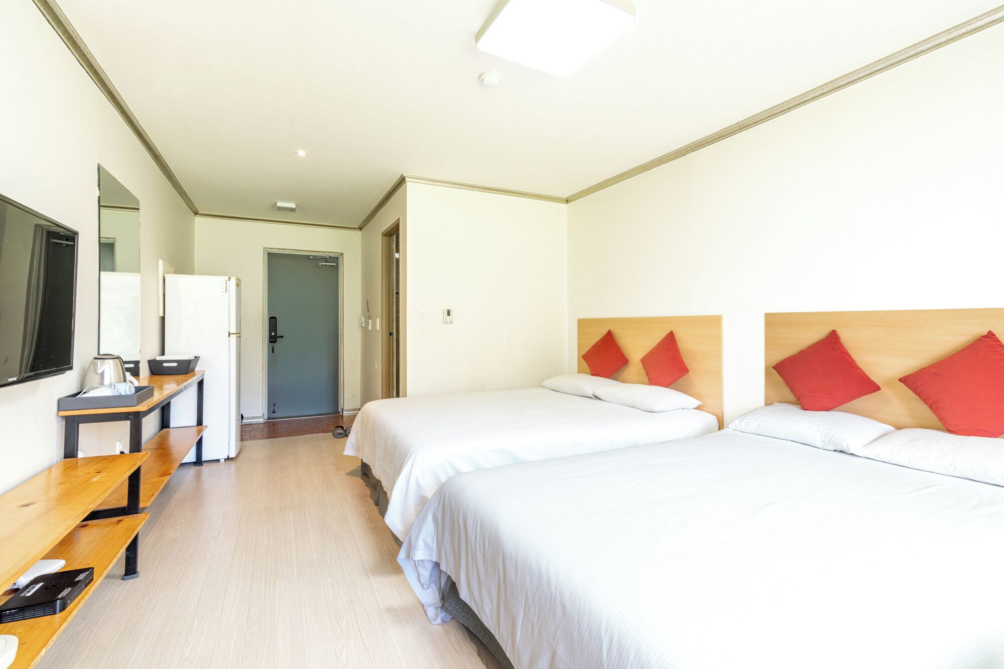Une chambre d’hôtel avec deux lits, un bureau, un miroir et une porte donnant sur une autre pièce.