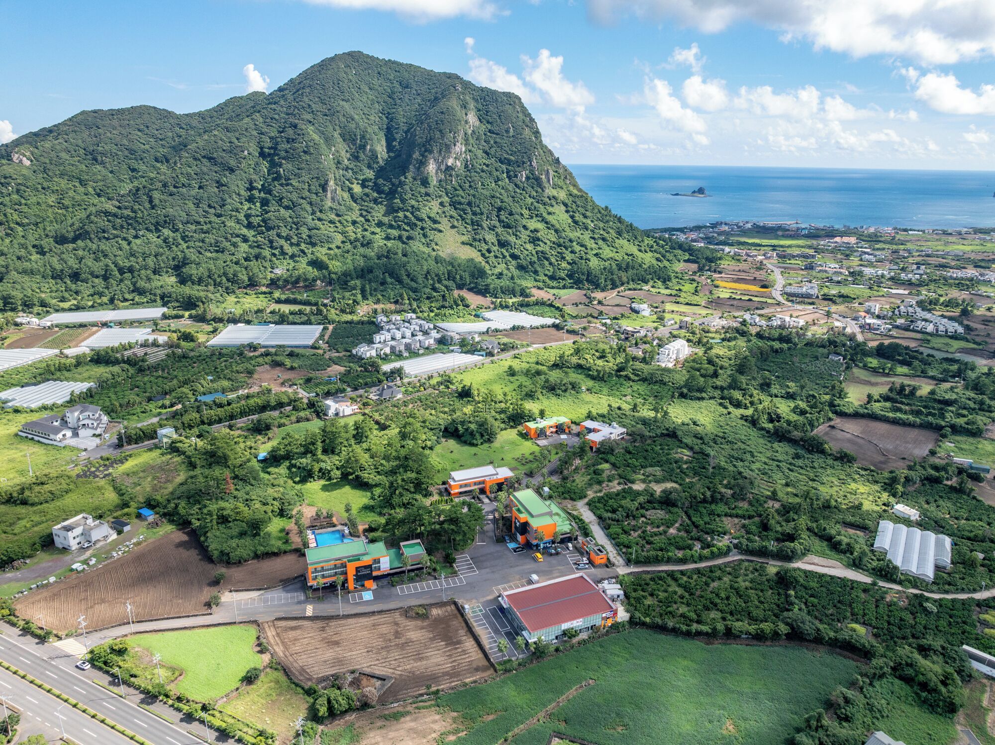 An aerial view of a rural area with a large mountain, agricultural fields, and scattered buildings.