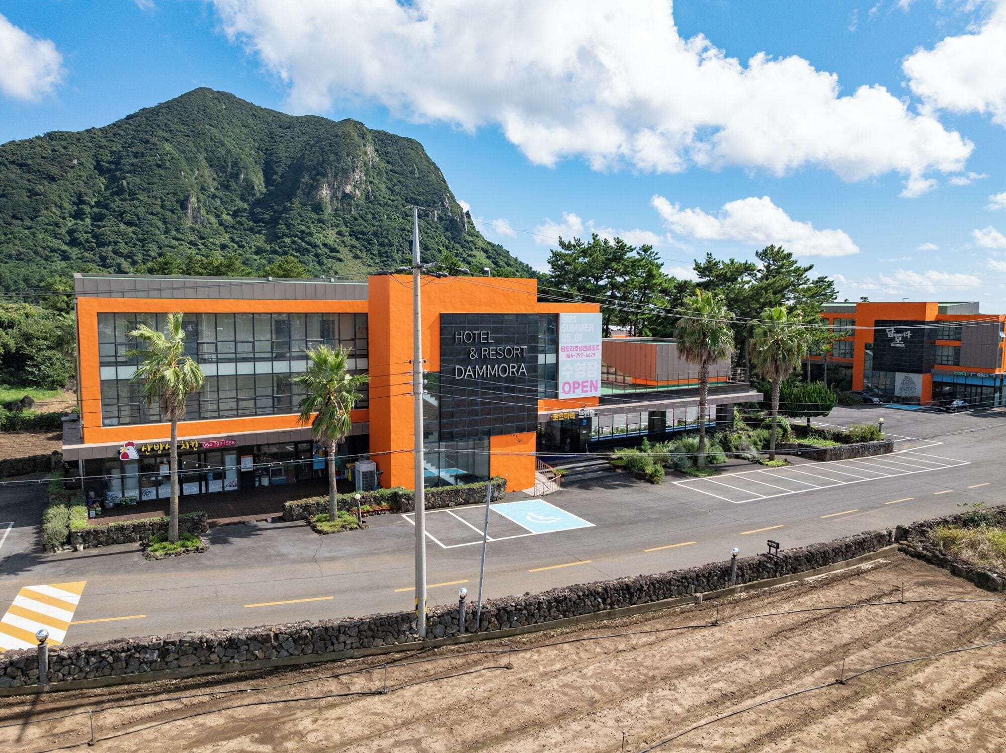 A modern hotel with a prominent orange facade, a parking lot, and a mountain in the background.