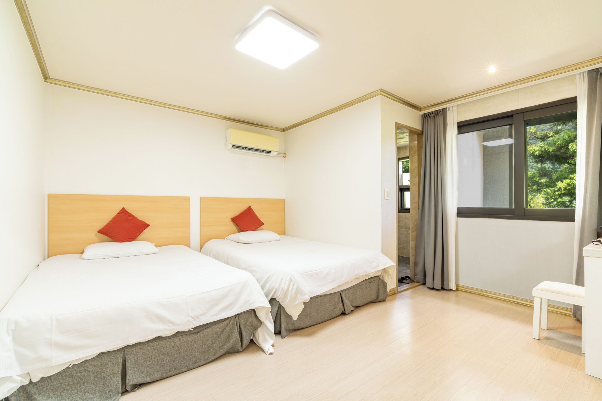 A hotel room with two beds, a desk, and a window with a view of greenery.