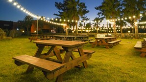 Un espacio al aire libre con mesas de picnic y luces colgantes.