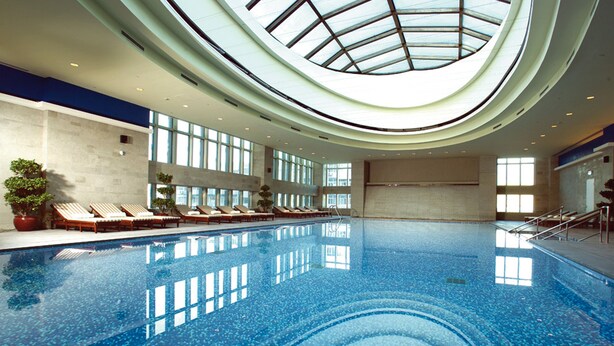 A large indoor swimming pool with a skylight, sun loungers, and potted plants. - Teda, Tianjin-marriott Executive Apartments (Tianjin)