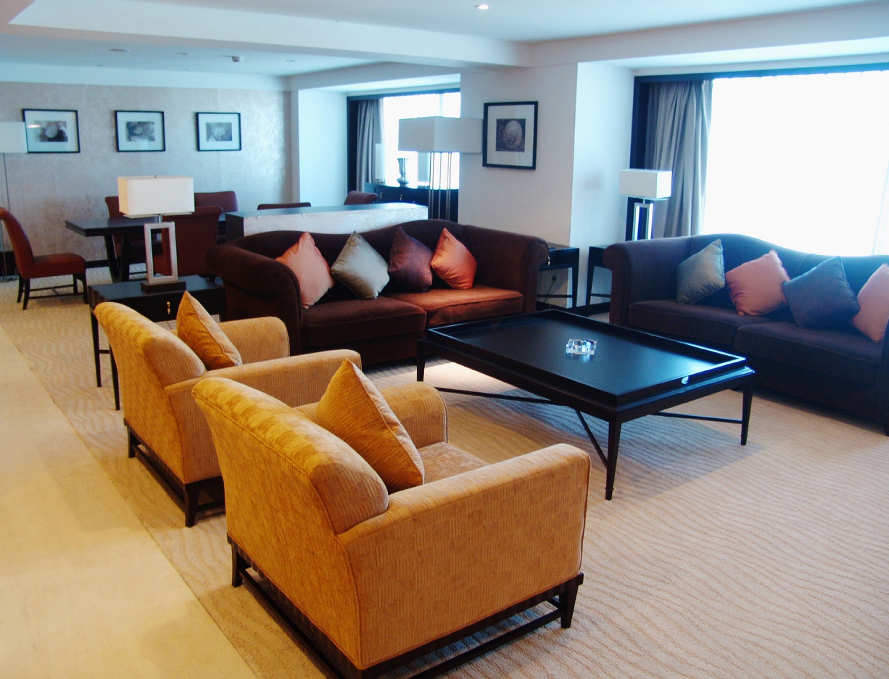 A spacious hotel room with a large sofa set, a coffee table, and a dining area with a table and chairs.