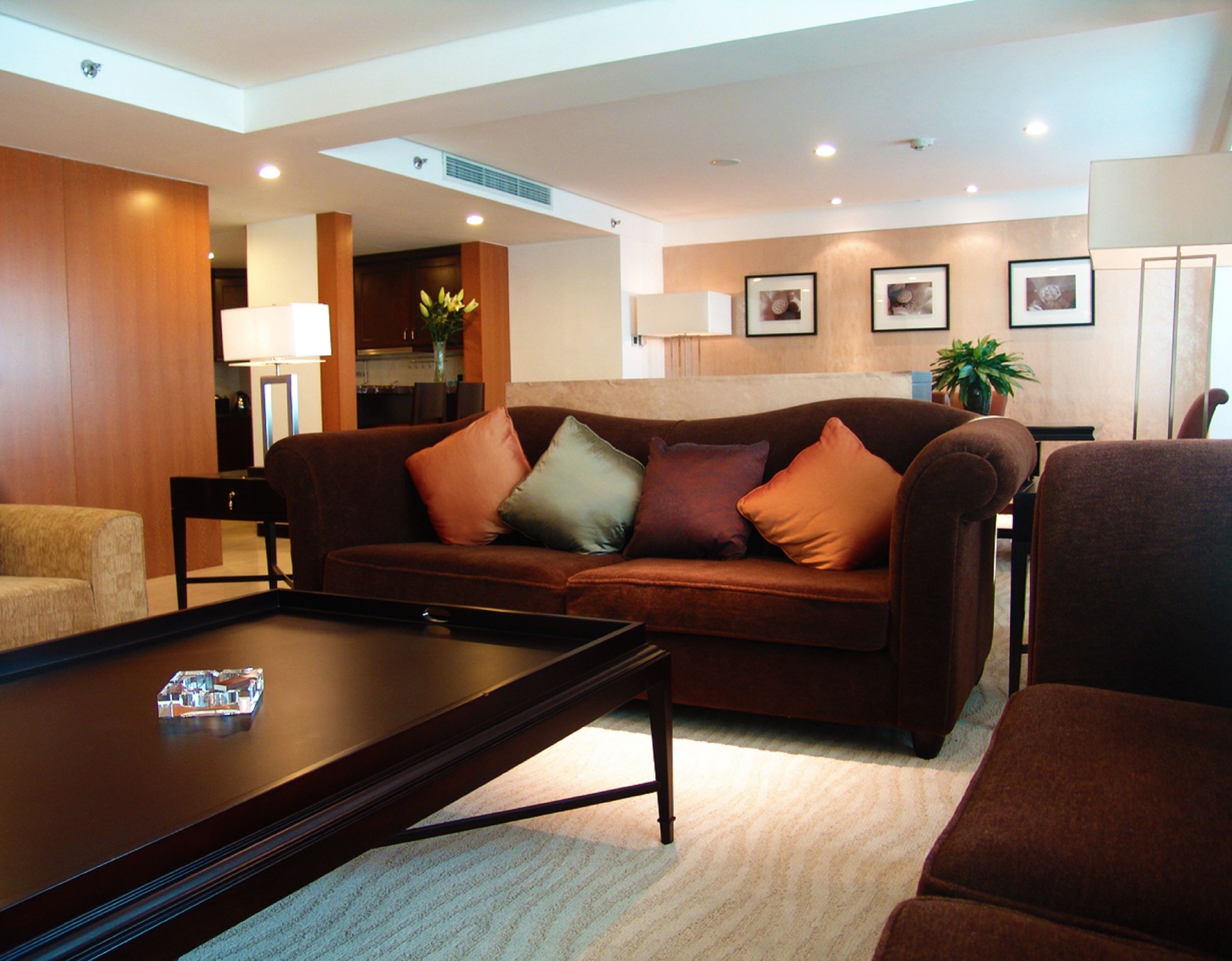 A modern living room with a brown sofa, a coffee table, and a dining area in the background.