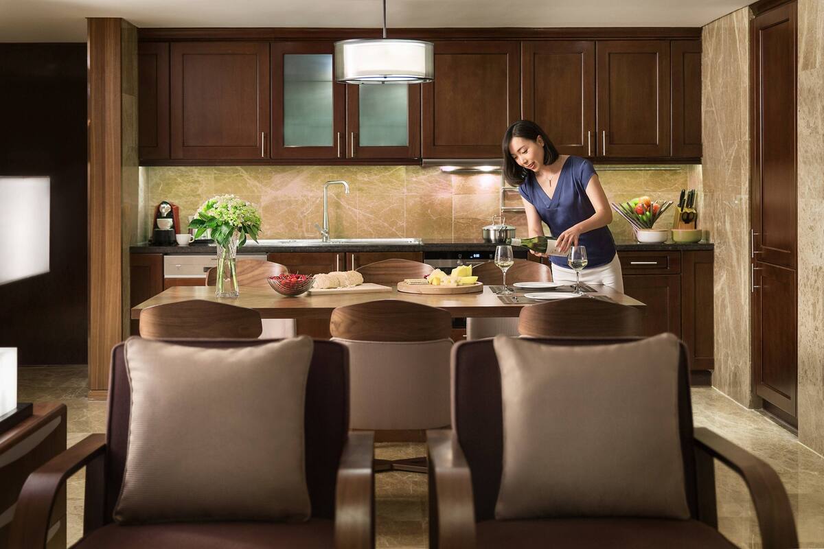 A modern kitchen with dark wooden cabinets, a marble backsplash, and a dining area with leather chairs.