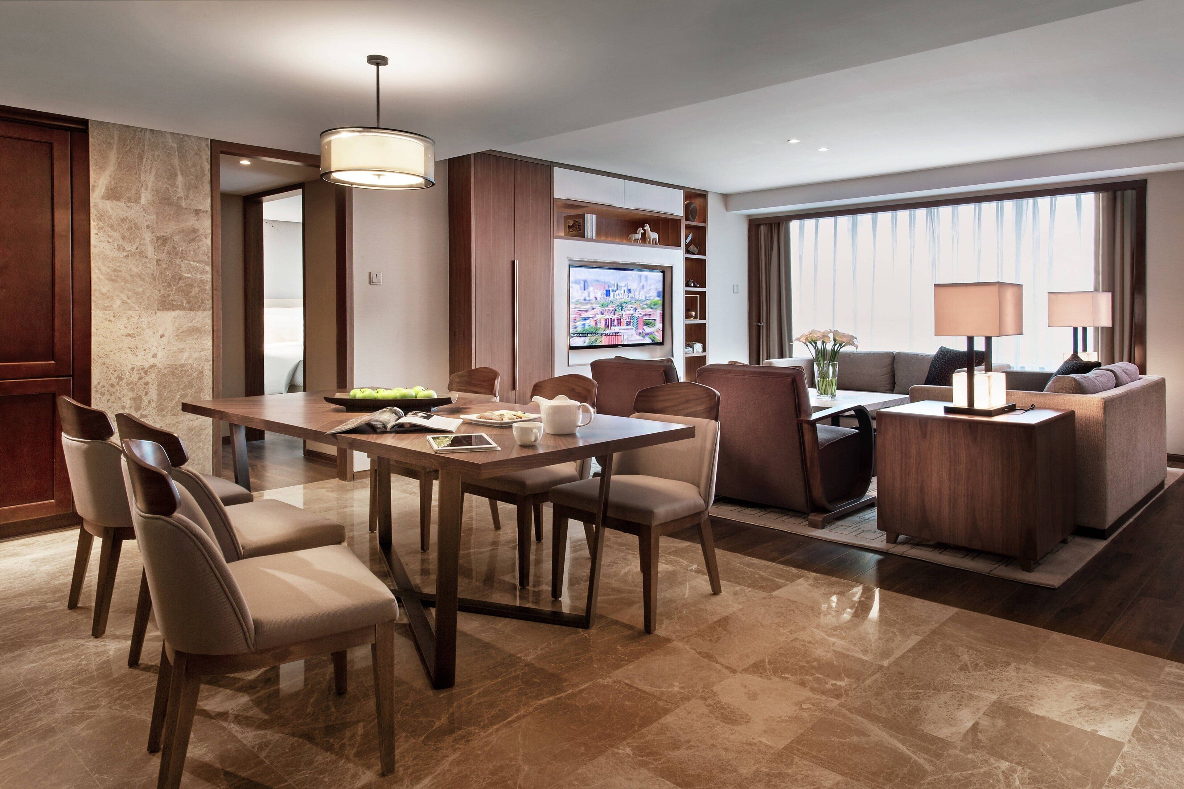 Quarto de hotel moderno com área de refeições, um sofá e uma TV.