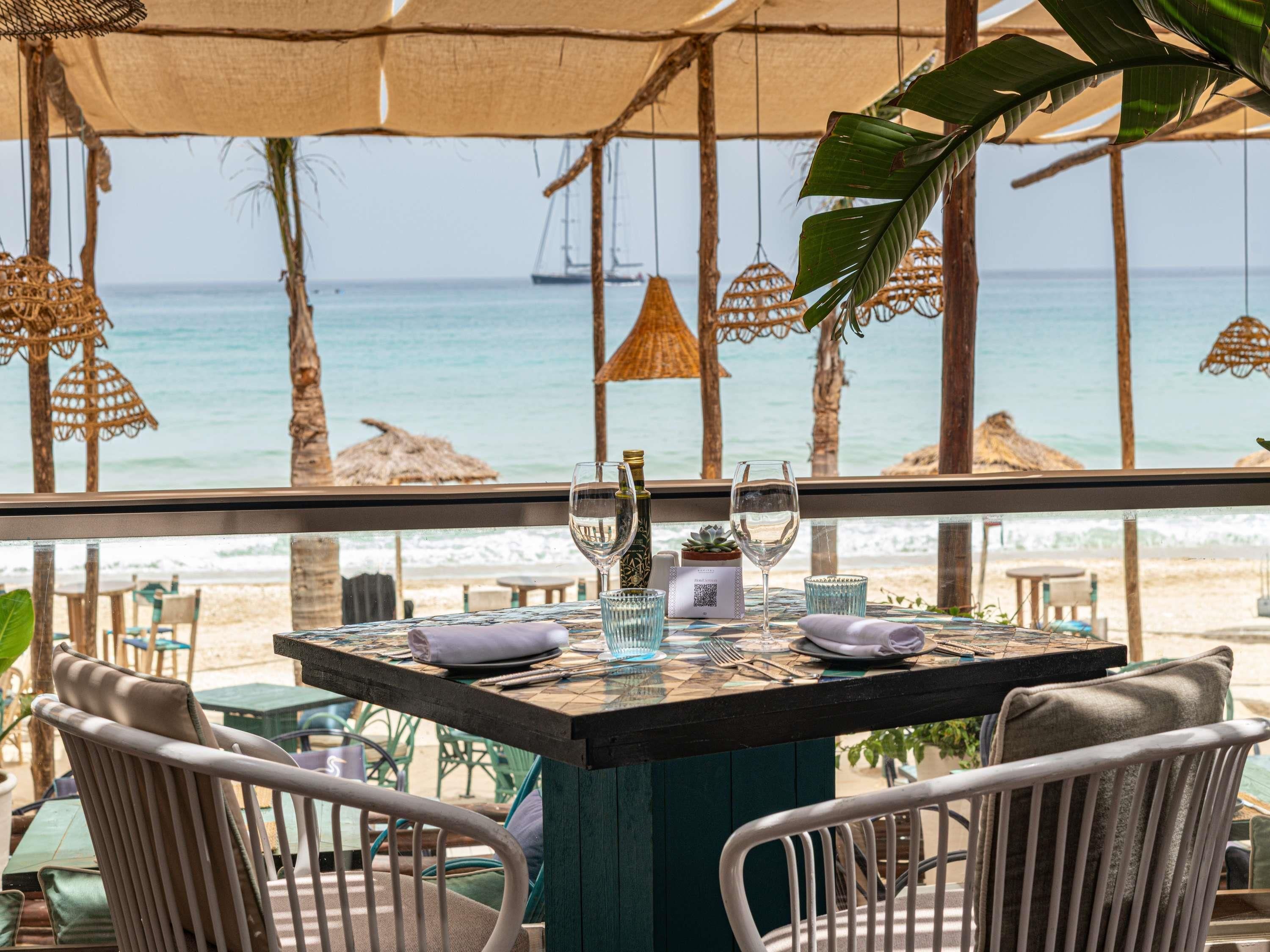 A table set for two with a view of the ocean and beach.