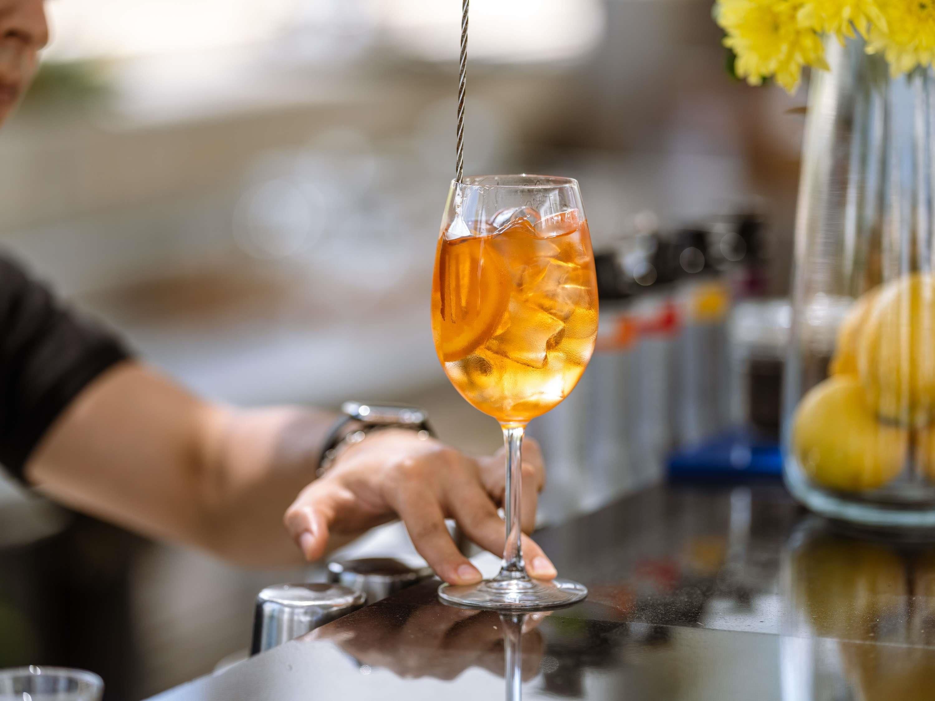 A person pouring a drink into a glass with ice cubes.