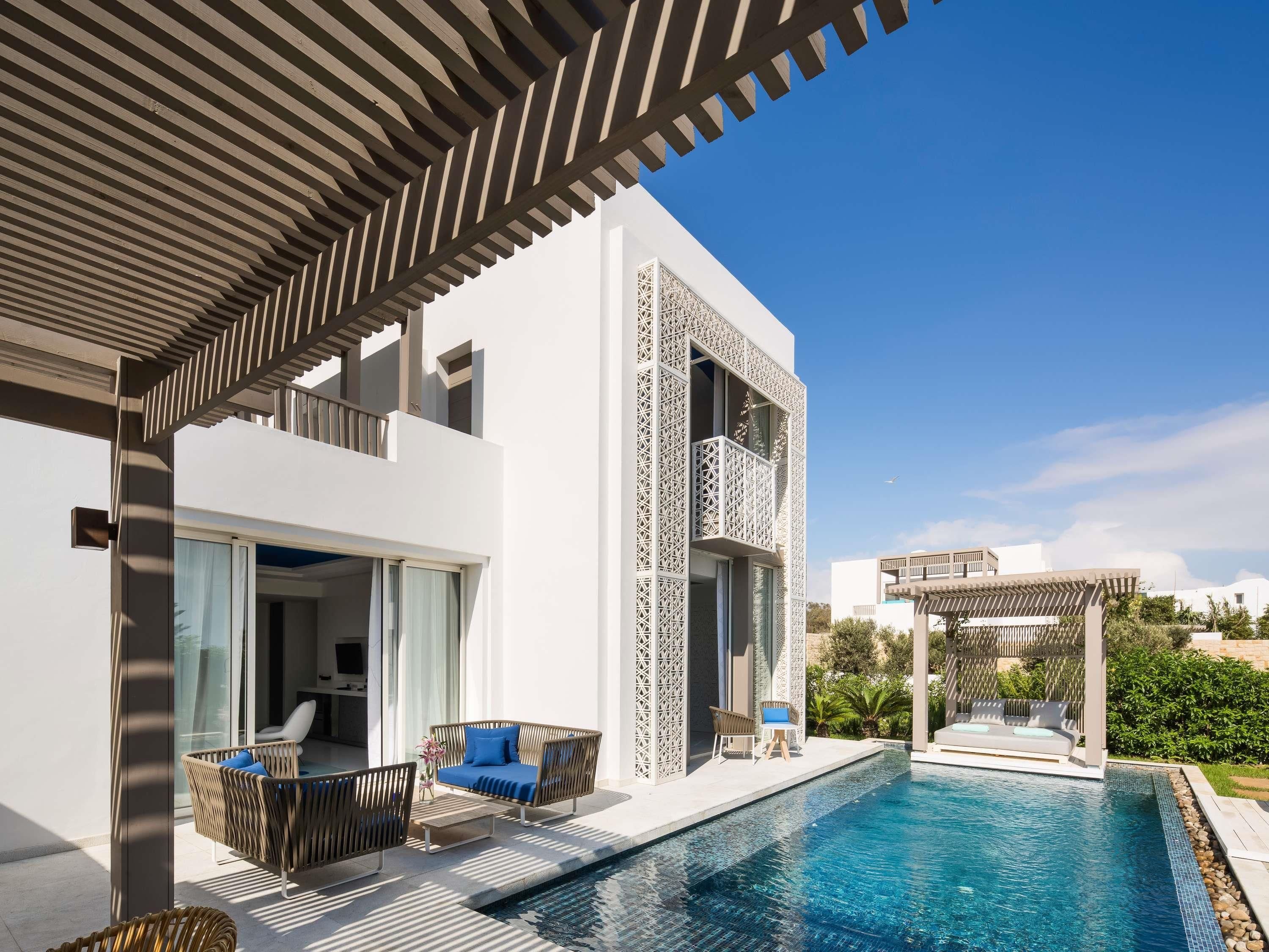 Una casa moderna con piscina, mobiliario exterior y una pérgola.