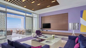 Una sala de estar moderna con televisor grande, asientos cómodos, un separador de vidrio y vistas al exterior.