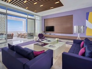 A modern living room with a large TV, comfortable seating, a glass partition, and a view of the outdoors. - Sofitel Tamuda Bay Beach and Spa (M'diq)