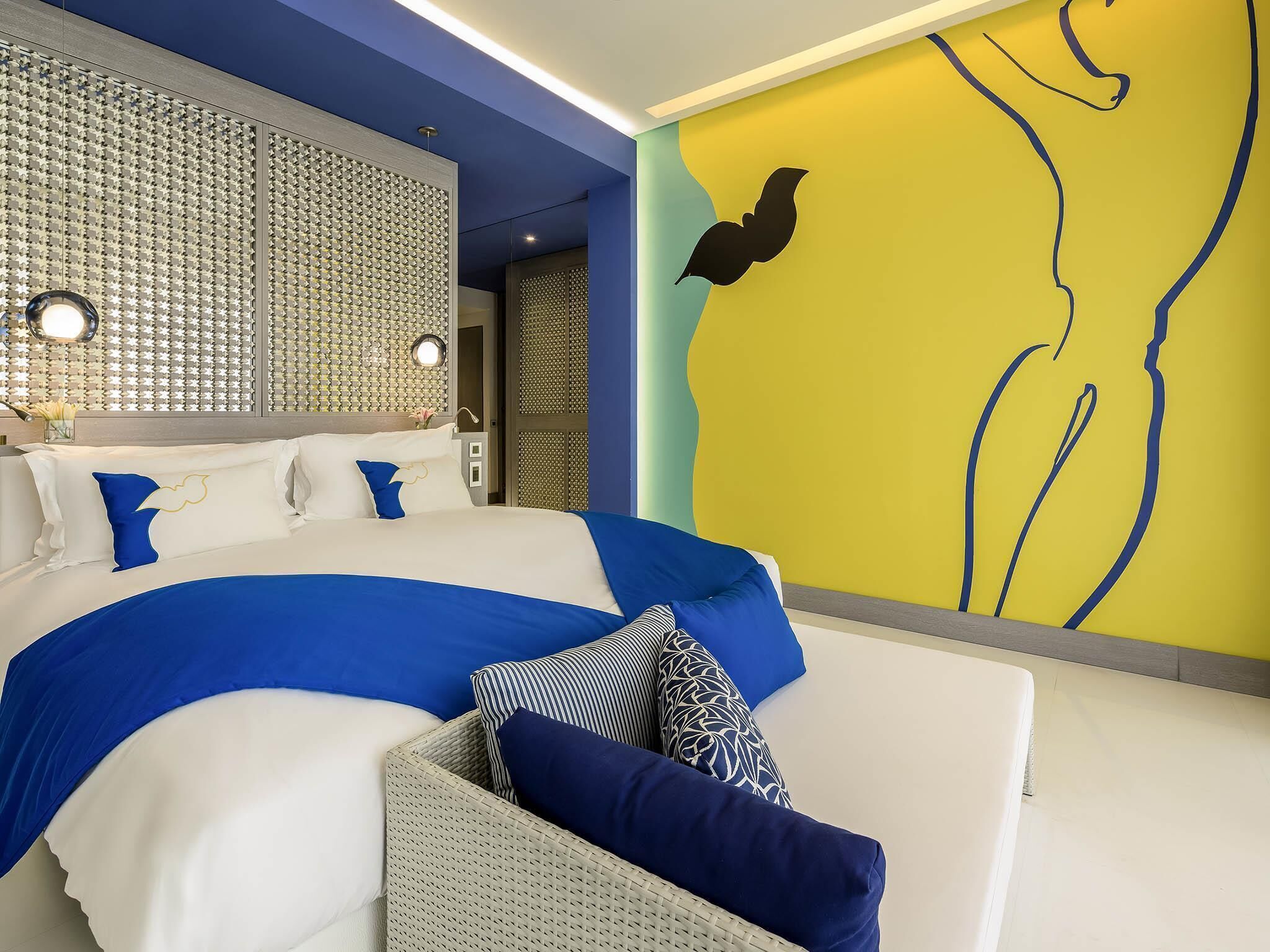 A modern hotel room with a large bed, a seating area, and a decorative wall.