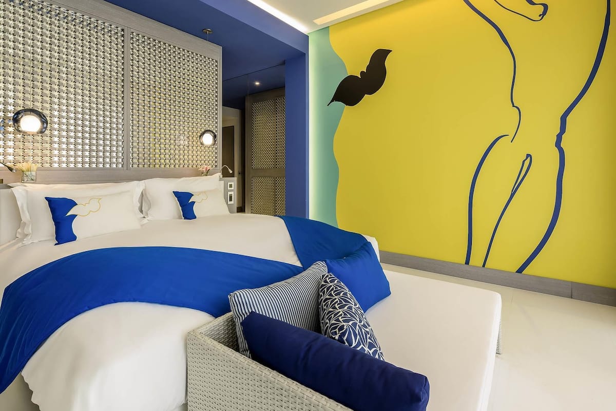 A modern hotel room with a large bed, a seating area, and a decorative wall.