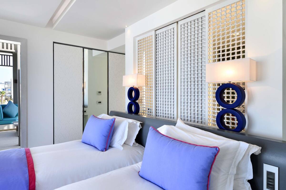 A hotel room with two beds, a large window with a decorative screen, and a view of the cityscape.