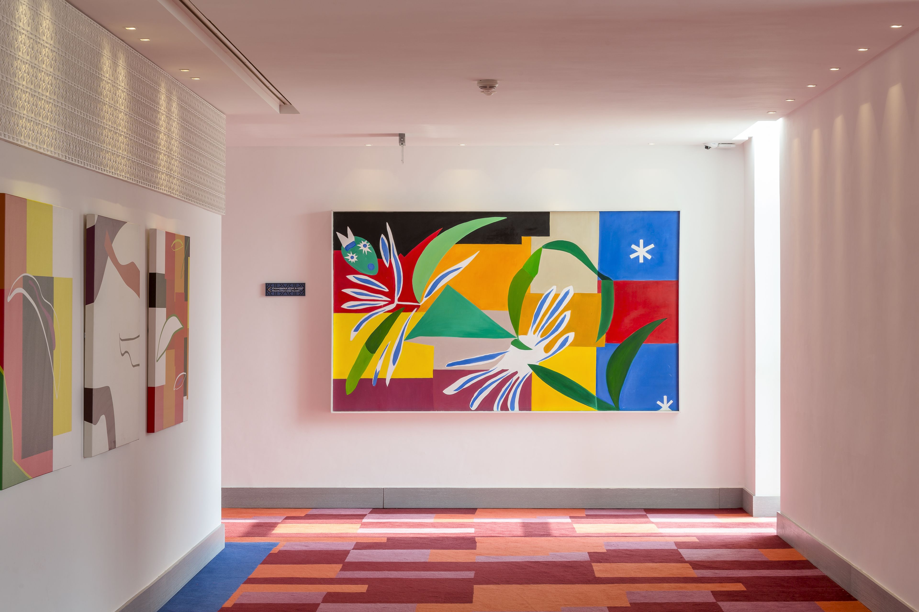 A hallway with a colorful abstract painting on the wall, a patterned ceiling, and a multicolored carpet.