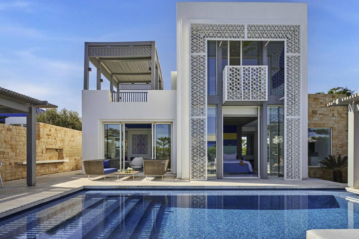 A modern two-story house with a swimming pool, large windows, and a balcony.