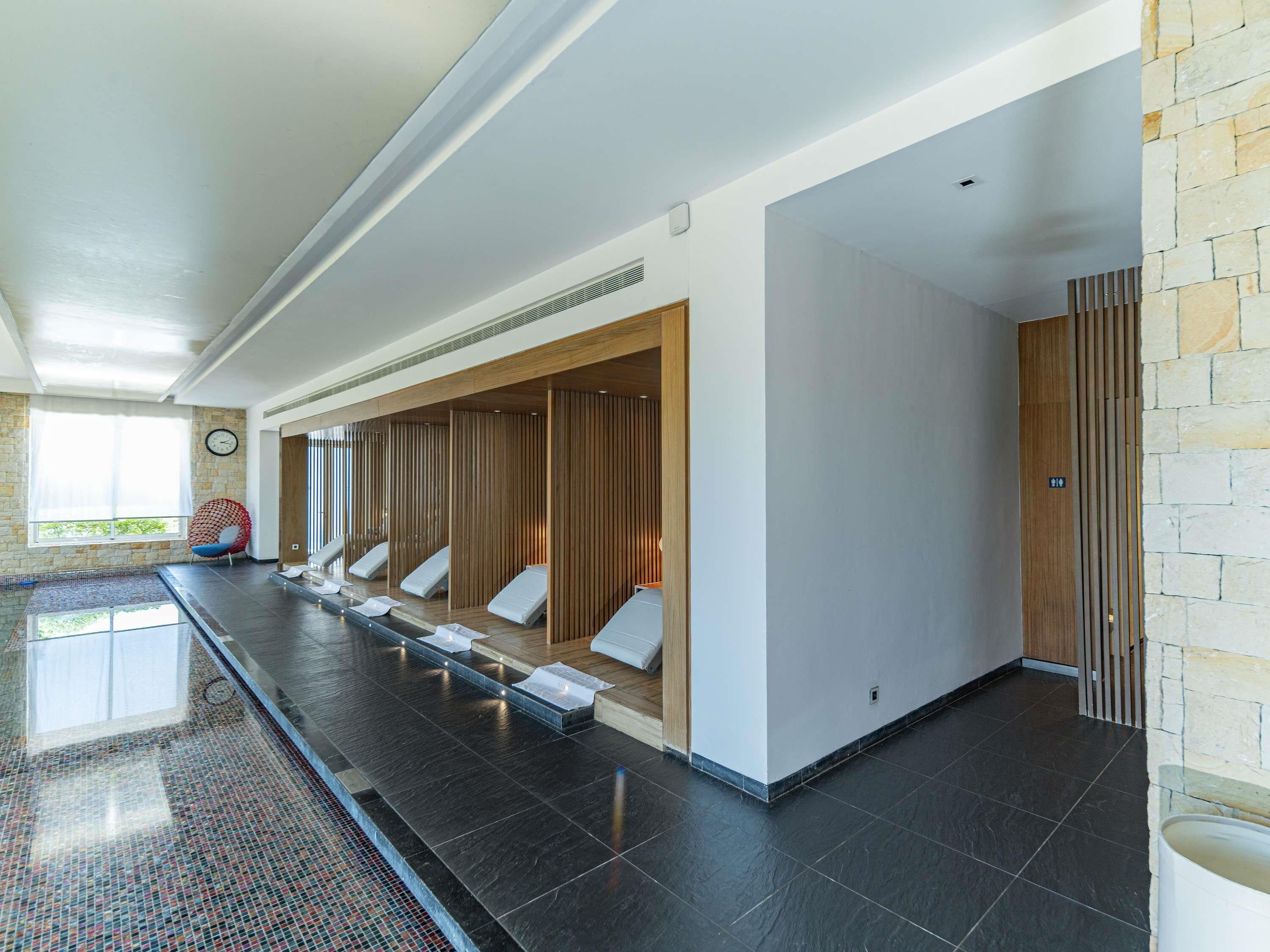 Un'area spa moderna con una lunga panca, separé in legno e una parete in pietra.