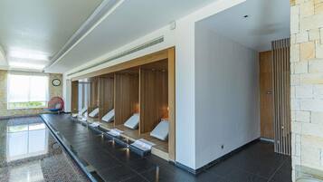 Un'area spa moderna con una lunga panca, separé in legno e una parete in pietra.
