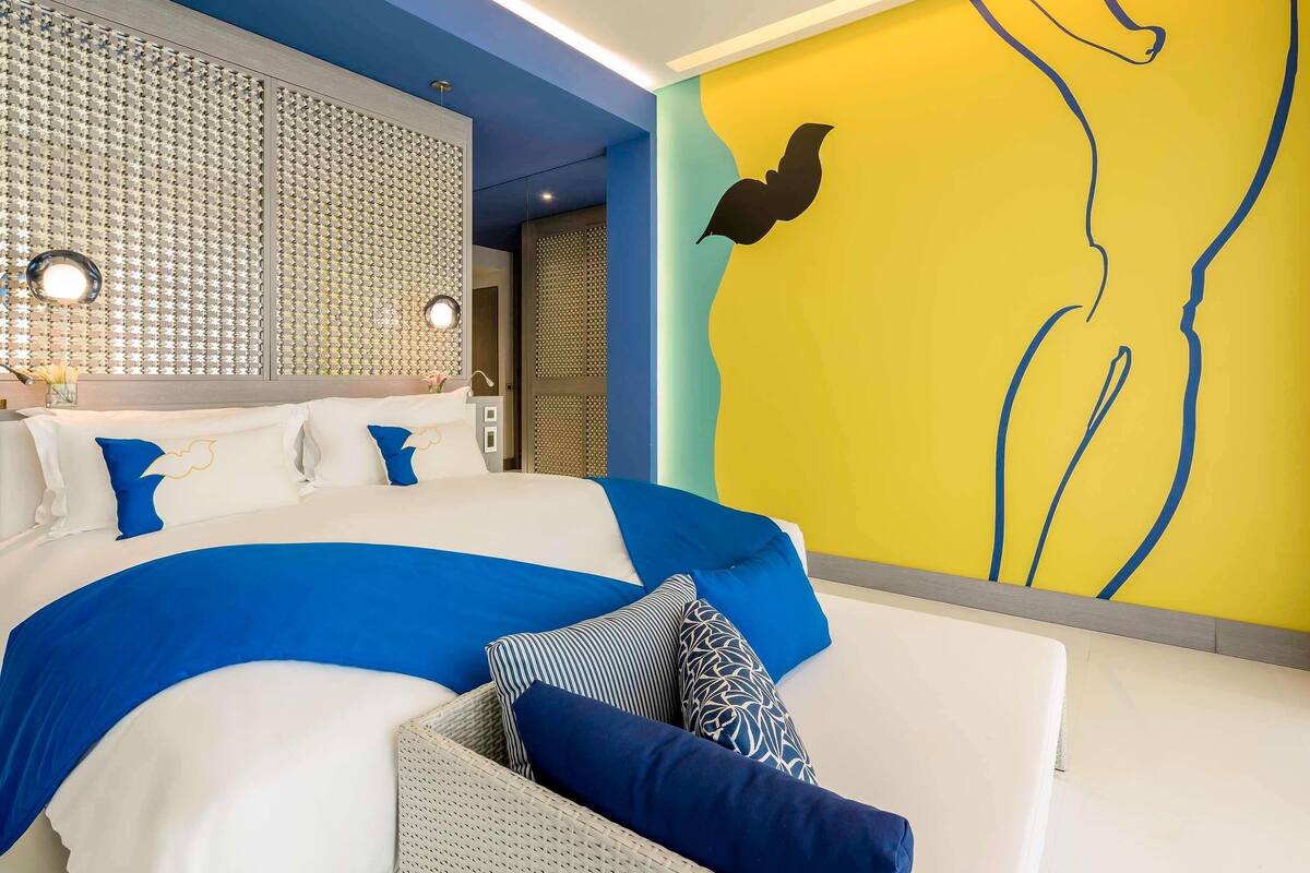 A modern bedroom with a large bed, a wall with a yellow mural, and a unique textured wall panel.