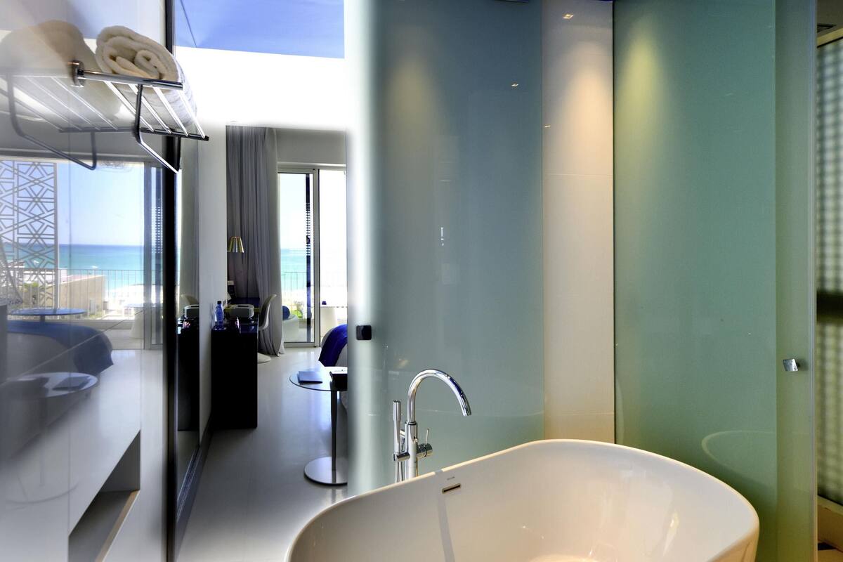Een moderne badkamer met een groot bad, een douchecabine van glas en uitzicht op zee.