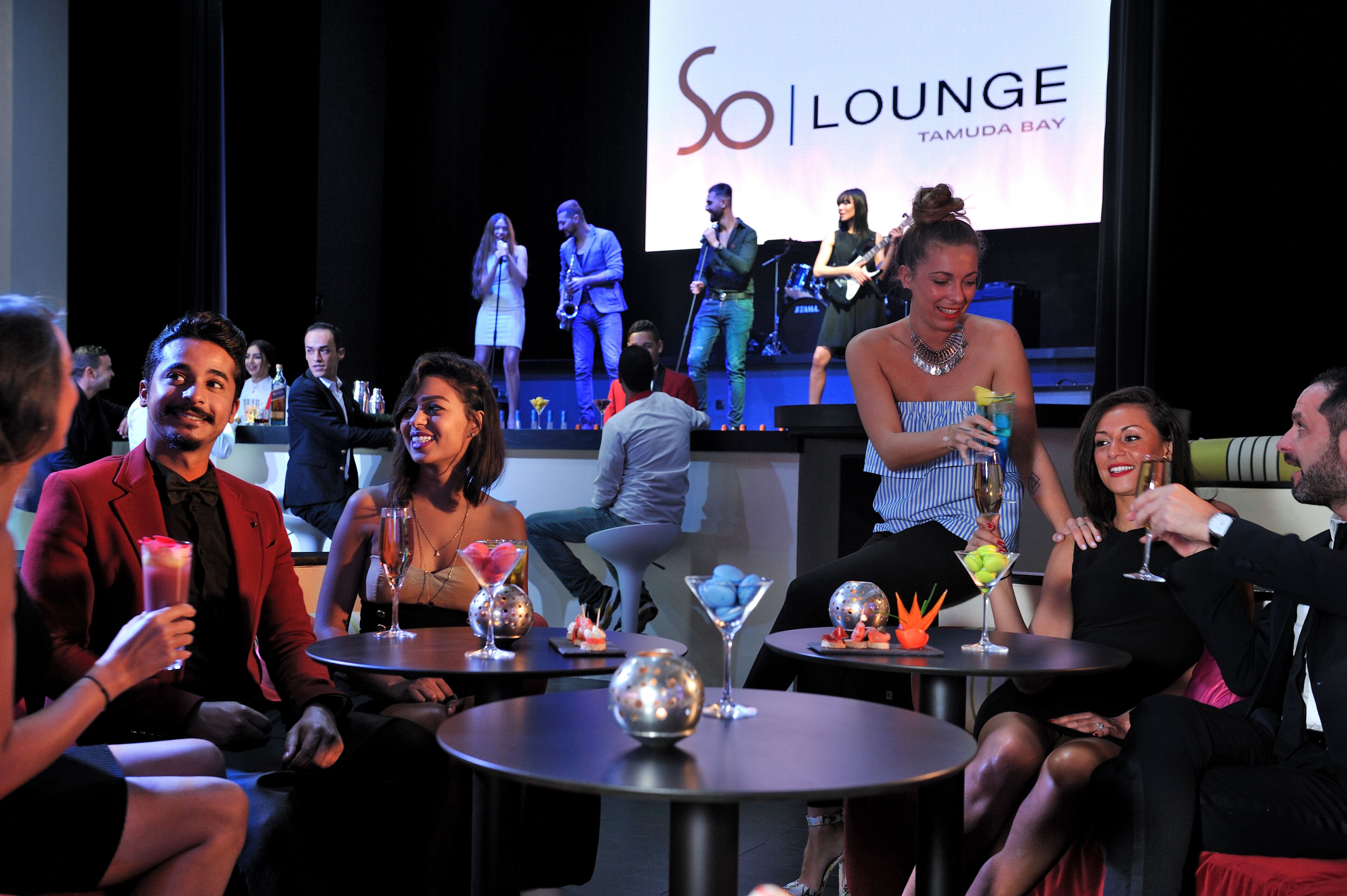 Evento So Lunge Tamuda Bay con escenario, asistentes sentados y mesas con bebidas y elementos decorativos.