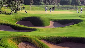 Play amidst undulating terrain and strategically placed sand bunkers surrounded by lush greenery and trees.