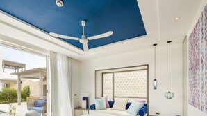 A modern living room with a blue ceiling, a ceiling fan, a sofa set, a dining table, and a view of the outdoors. - Sofitel Tamuda Bay Beach and Spa (M'diq)