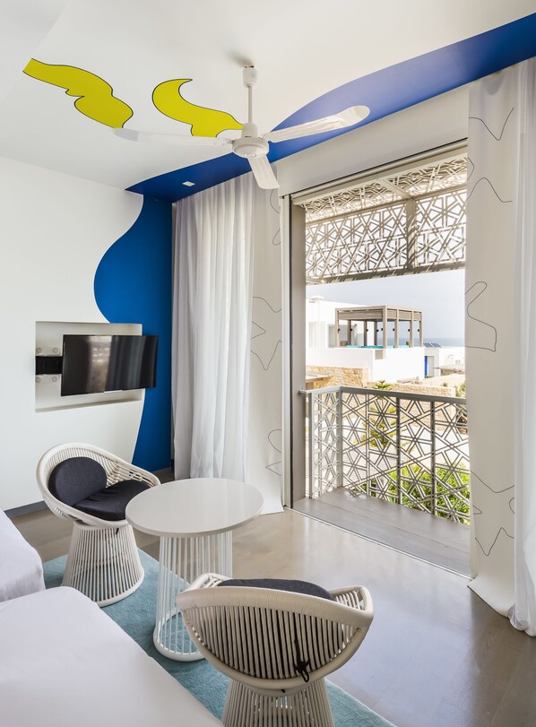 A modern room with a ceiling fan, a TV, a balcony with a view, and a seating area with a table and chairs.