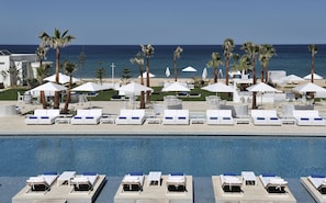 Zona de piscina d'un hotel amb gandules i ombrelles, vista despejada de l'oceà i un jardí ben cuidat.