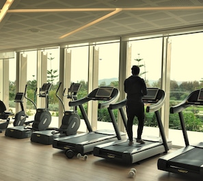 A gym with treadmills and exercise equipment, large windows, and a view of greenery. - Sofitel Tamuda Bay Beach and Spa (M'diq)