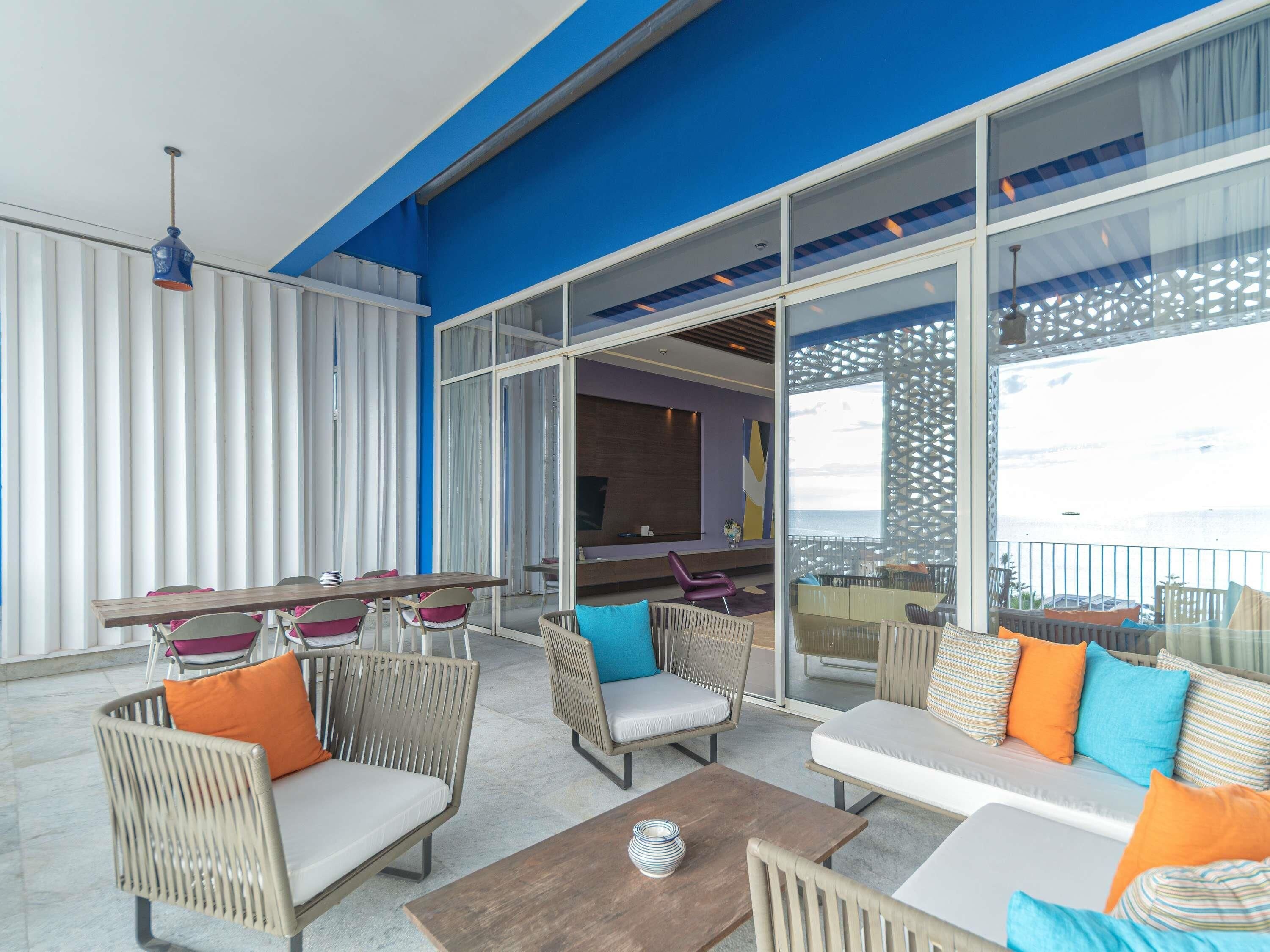 An outdoor seating area with wicker furniture, a wooden table, and a view of the sea.