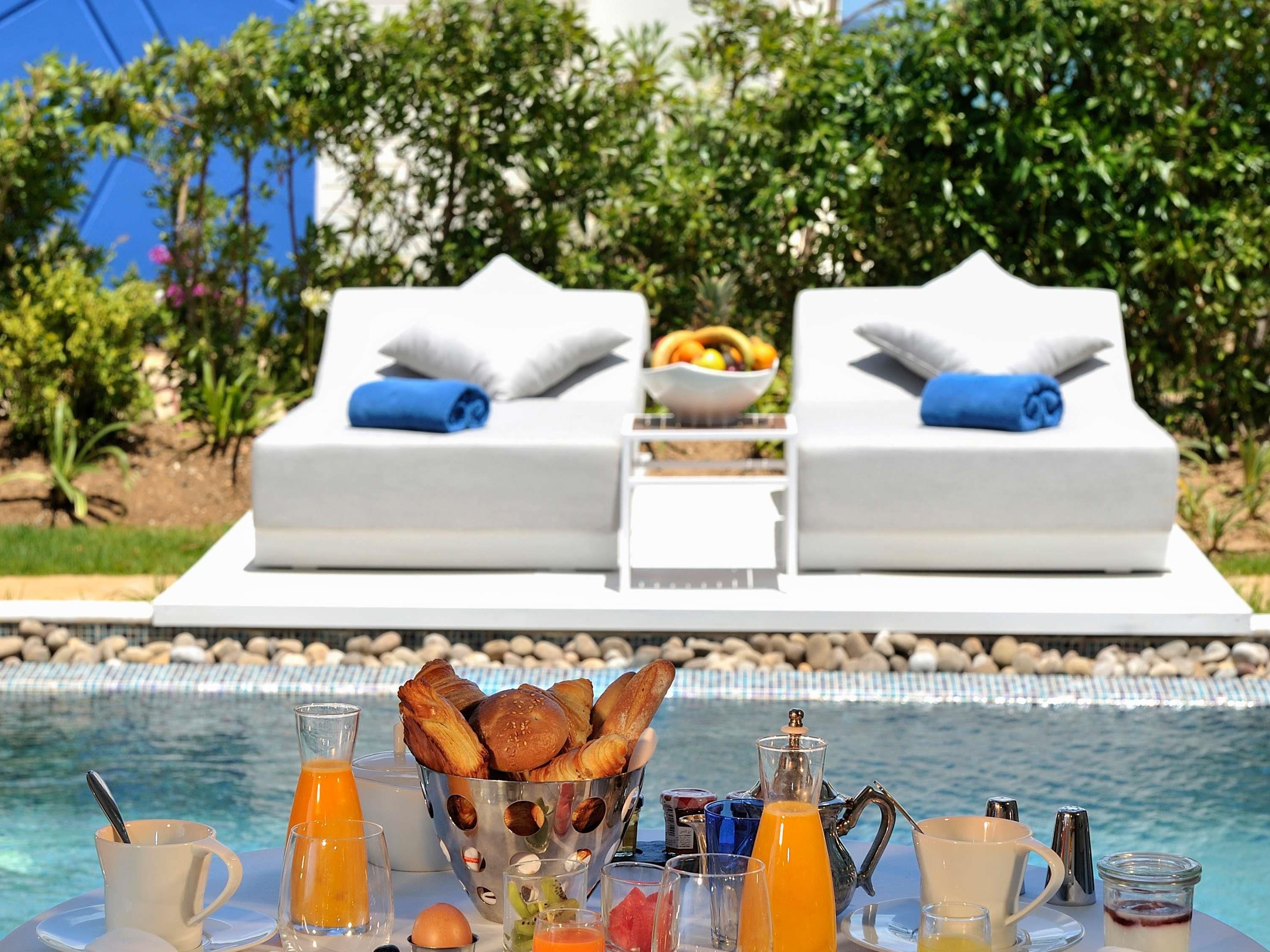 Desayuno junto a la piscina, con una mesa, alimentos para el desayuno y dos sillas reclinables con toallas.