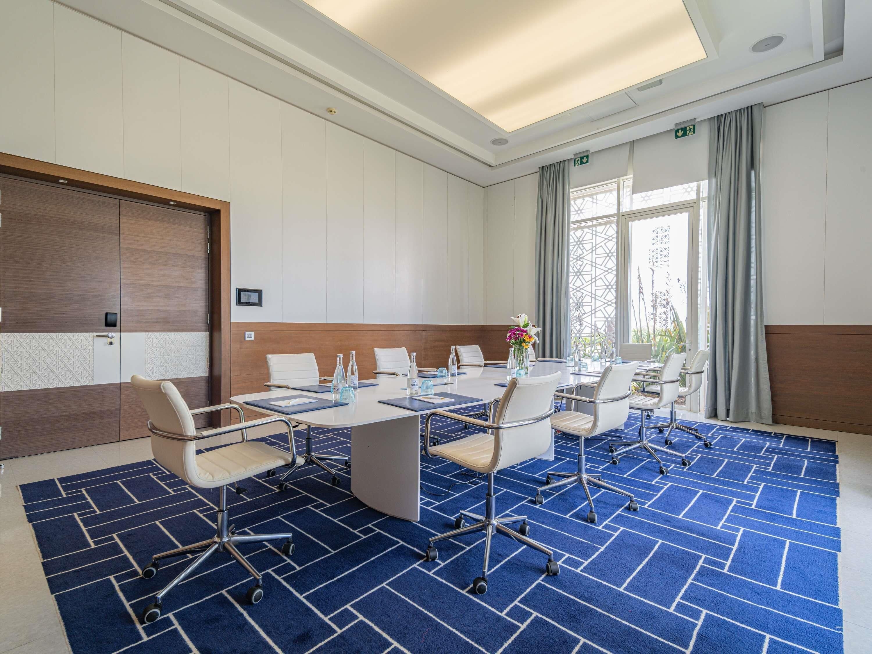 Une salle de conférence avec une grande table, des chaises et un tapis bleu à motifs.