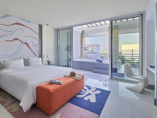 Una habitación de hotel moderna con una cama grande, un balcón con vistas y una zona de estar con una silla.