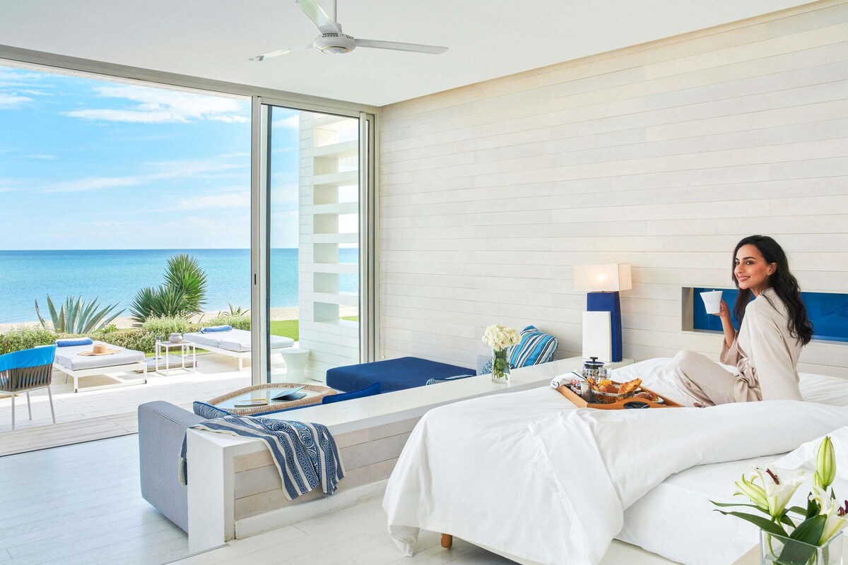 A modern hotel room with a large bed, a seating area with a view of the sea, and a balcony.