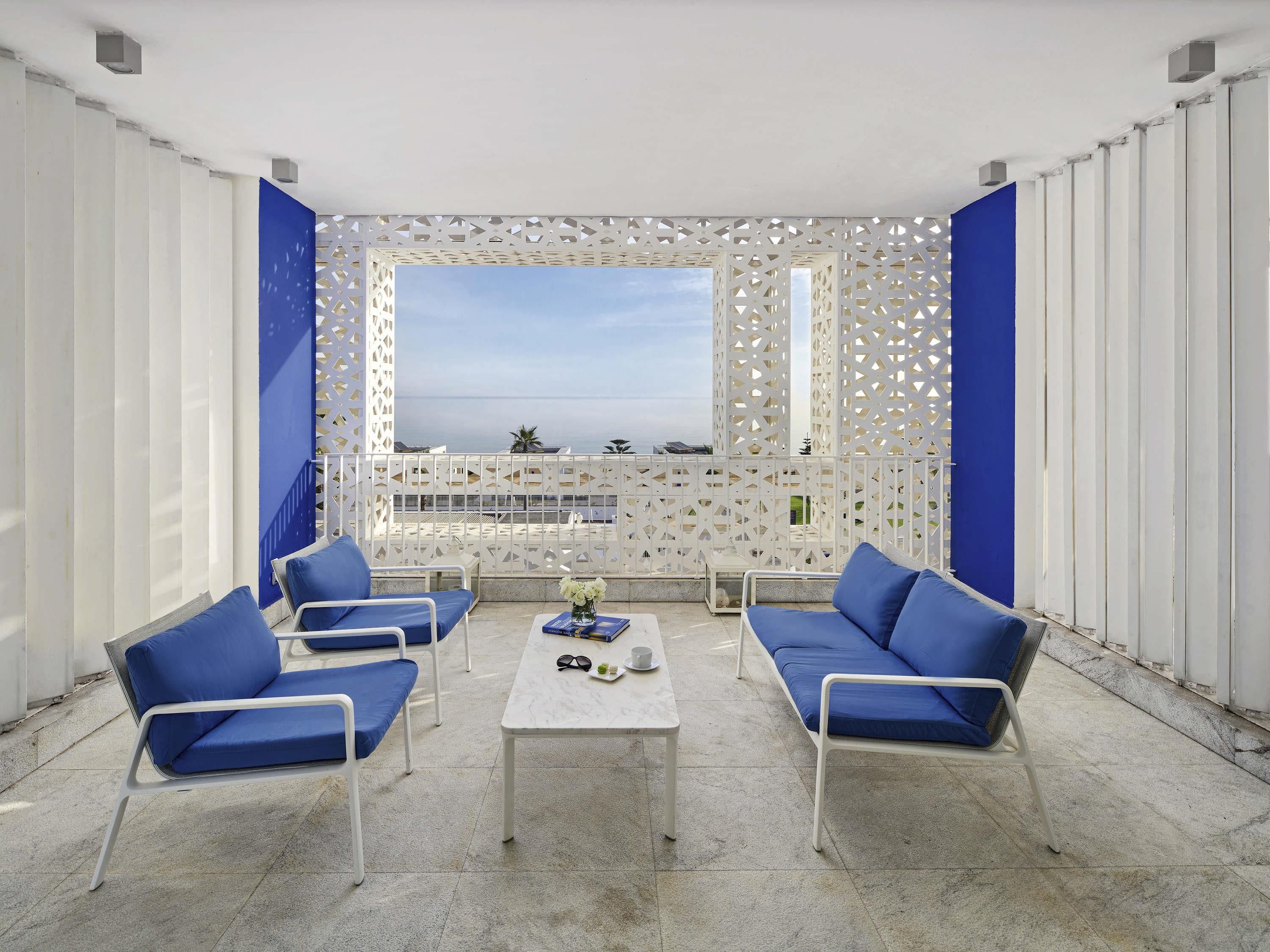 A terrace with white and blue furniture, a white table, and a view of the sea.
