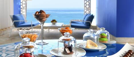 Una mesa servida con diversos postres y vista al mar.