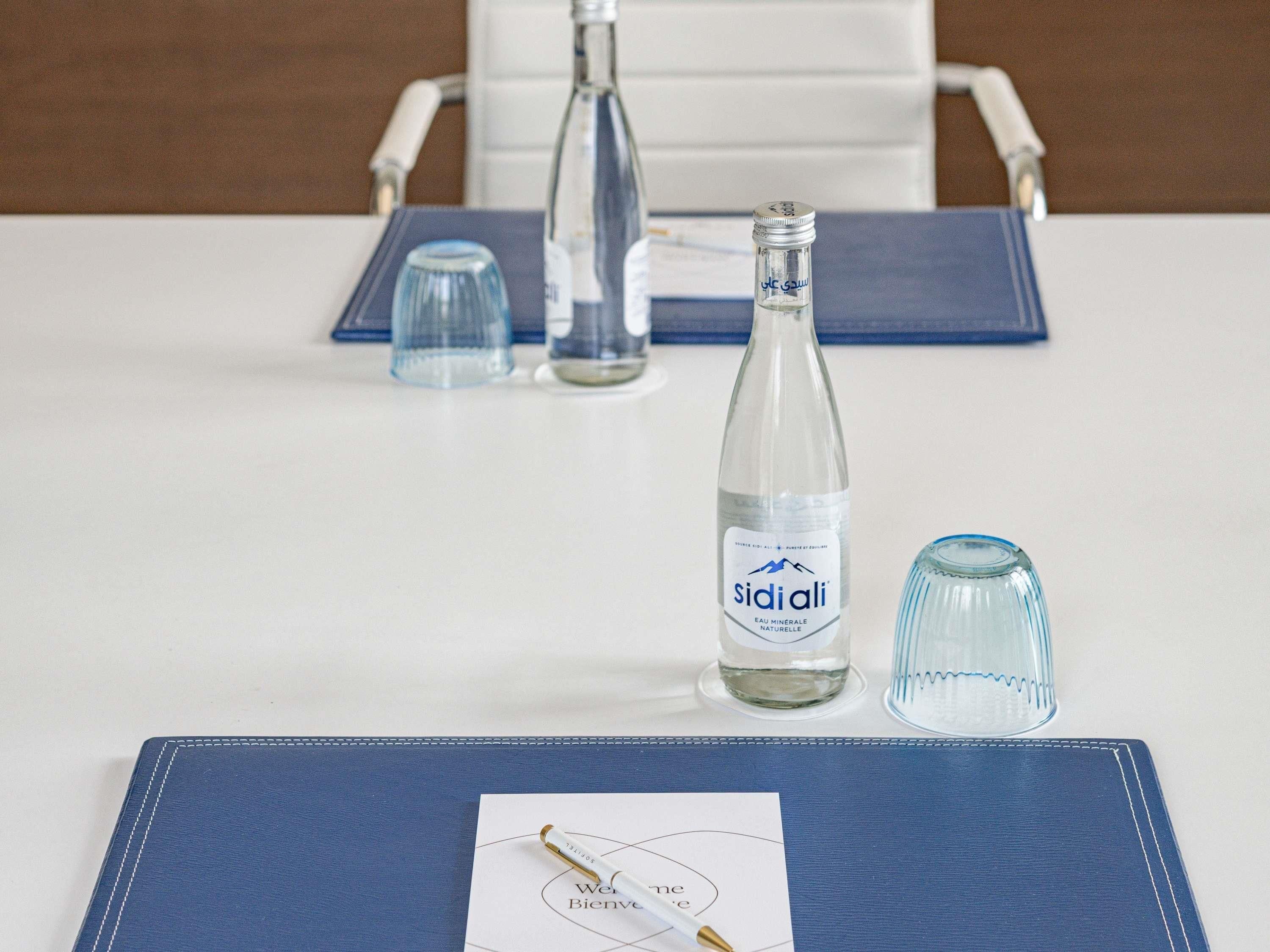 Una mesa con un cuaderno, un bolígrafo, una botella de agua Sidiali y dos vasos.